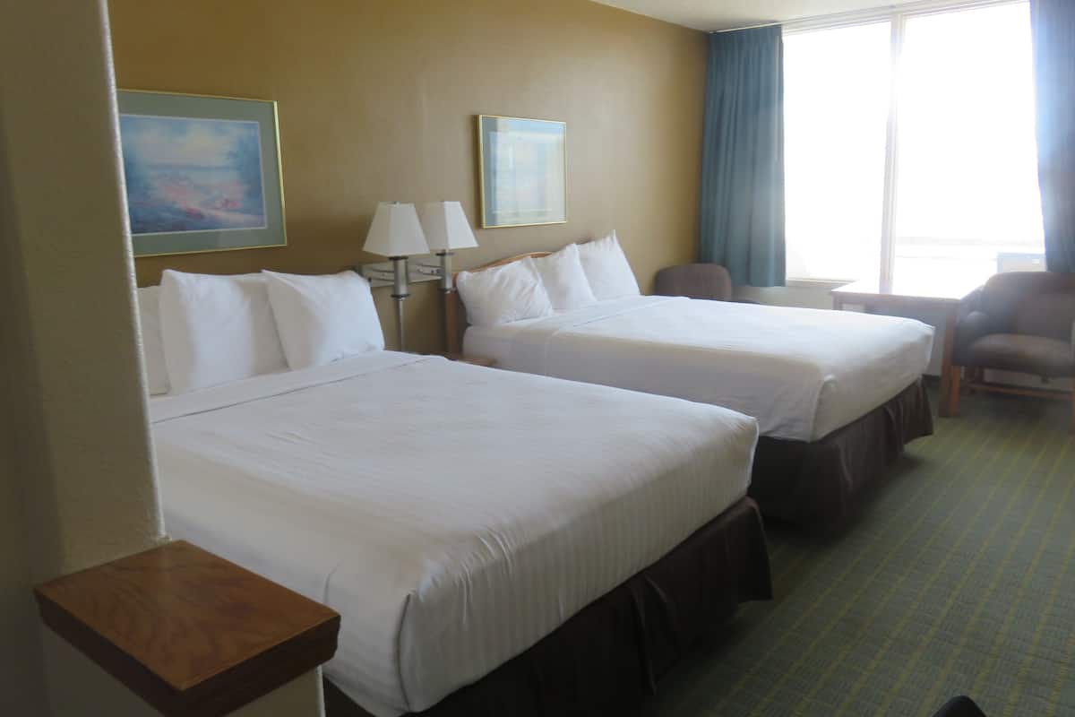 A hotel room with two beds, a desk, a chair, and a window with curtains.