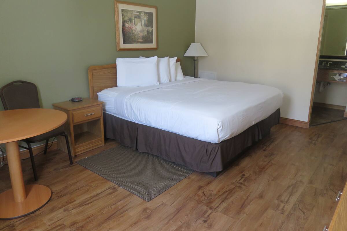 A neatly arranged hotel room with a bed, bedside table, lamp, chair, and a small table.