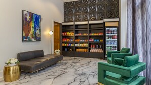 A lobby with a marble floor, a sofa, a green armchair, a bookshelf with snacks, and a refrigerator. - Hotel Gibbs Downtown Riverwalk (San Antonio)