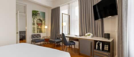 A hotel room with a bed, desk, chair, TV, and coffee machine.
