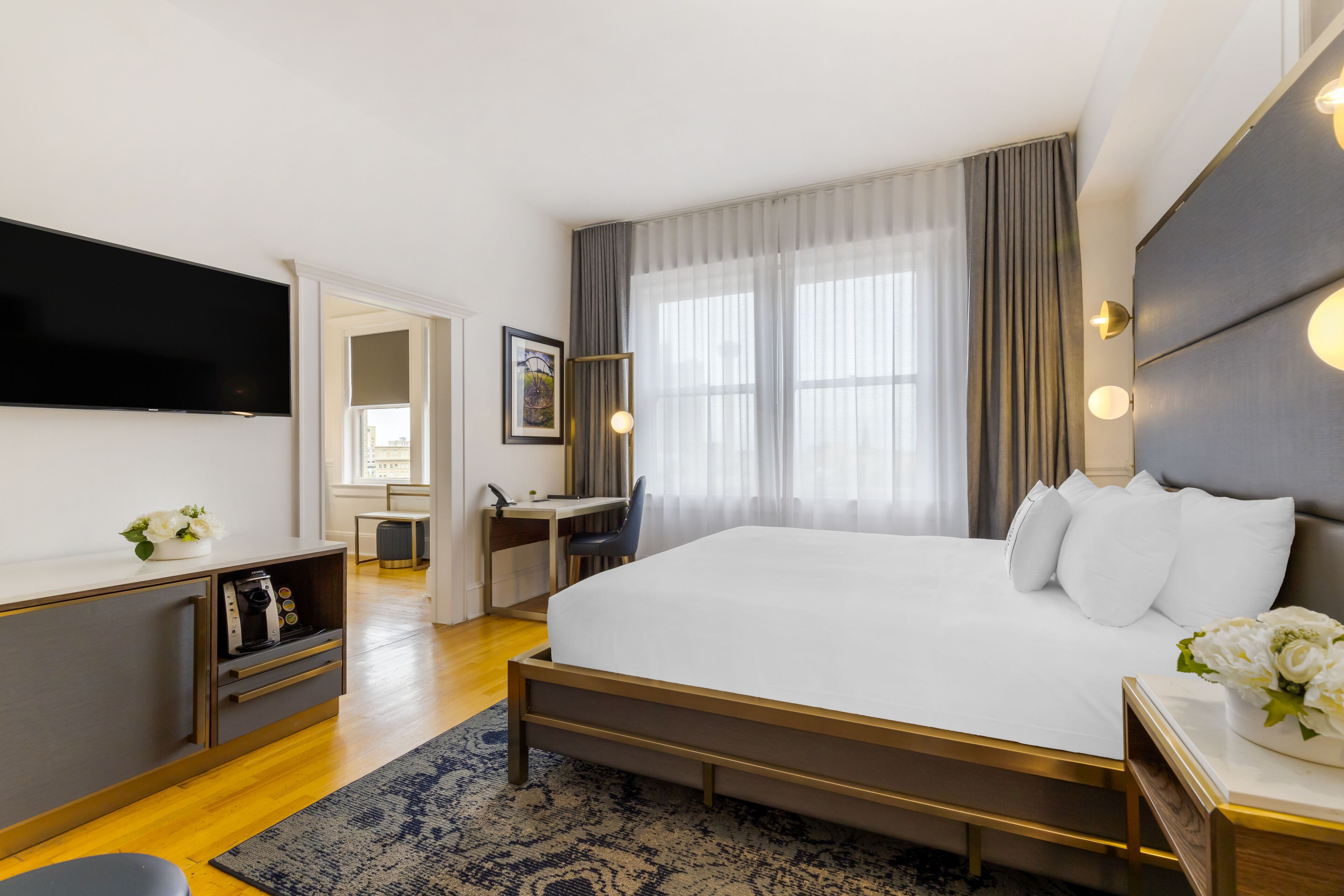 Habitación de hotel moderna con una cama grande, un escritorio, un televisor de pantalla plana y vistas a la ciudad a través de amplias ventanas.