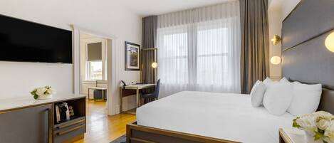 Habitación de hotel moderna con una cama grande, un escritorio, un televisor de pantalla plana y vistas a la ciudad a través de amplias ventanas.