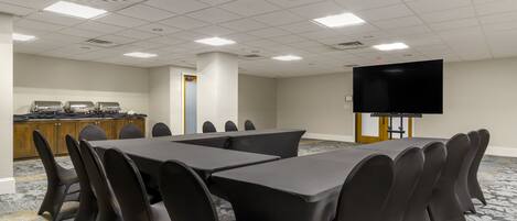 Une salle de conférence équipée d’une longue table, de chaises, d’un écran de projection et d’un coin cuisine.