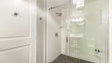 Une salle de bain moderne avec une douche à l’italienne en verre, des murs recouverts de carreaux blancs et un sol à motifs.