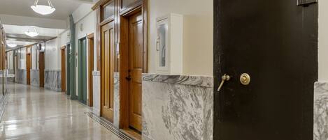 A long, polished hallway with marble flooring, wooden doors, and a black door with a brass handle.