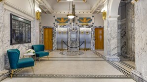 A lobby with marble floors, teal chairs, and a central elevator. - Hotel Gibbs Downtown Riverwalk (San Antonio)