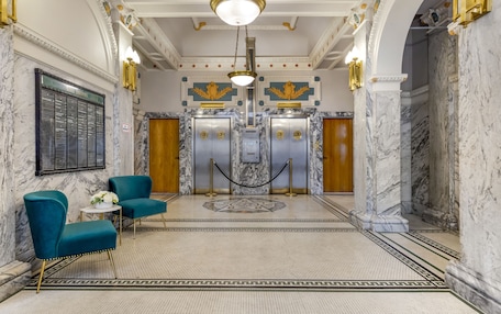 A lobby with marble floors, teal chairs, and a central elevator.