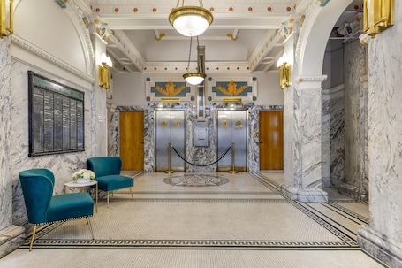 A lobby with marble floors, teal chairs, and a central elevator.