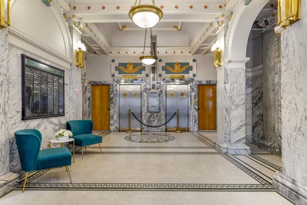 A lobby with marble floors, teal chairs, and a central elevator.