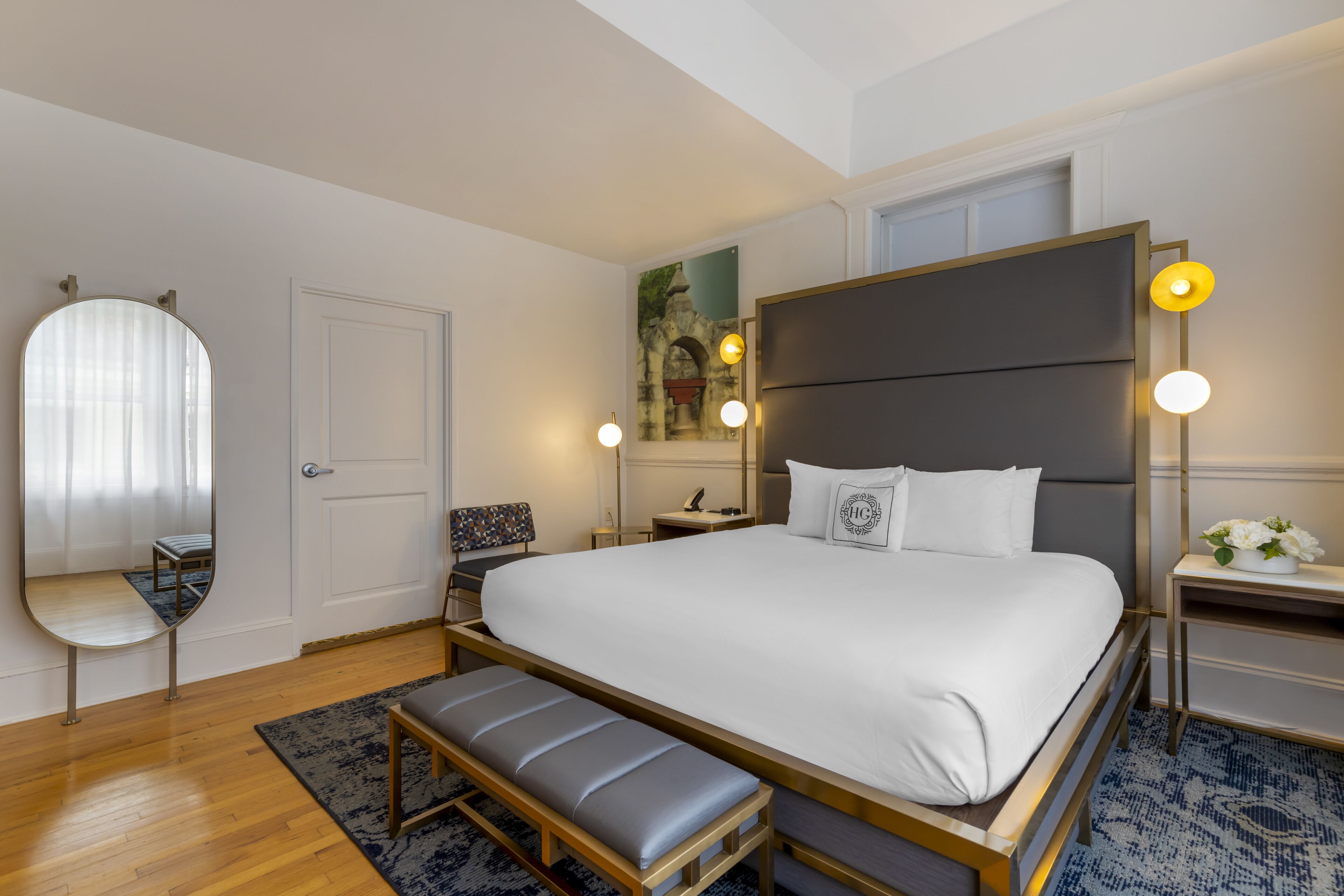Une chambre d’hôtel moderne avec un grand lit, un banc, un miroir, un bureau et une table de chevet.