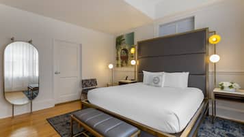 Ein modernes Hotelzimmer mit einem großen Bett, einer Bank, einem Spiegel, einem Schreibtisch und einem Nachttisch.