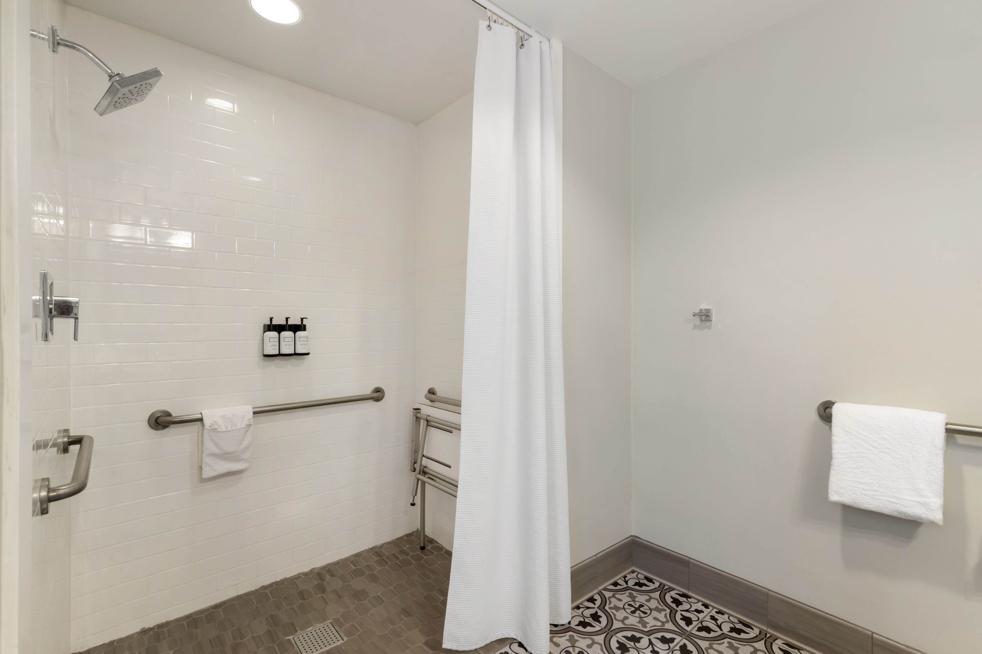 Une salle de bain moderne avec des murs carrelés de blanc, une douche équipée d’un pommeau de douche à main, d’une barre d’appui et d’un porte-serviettes.