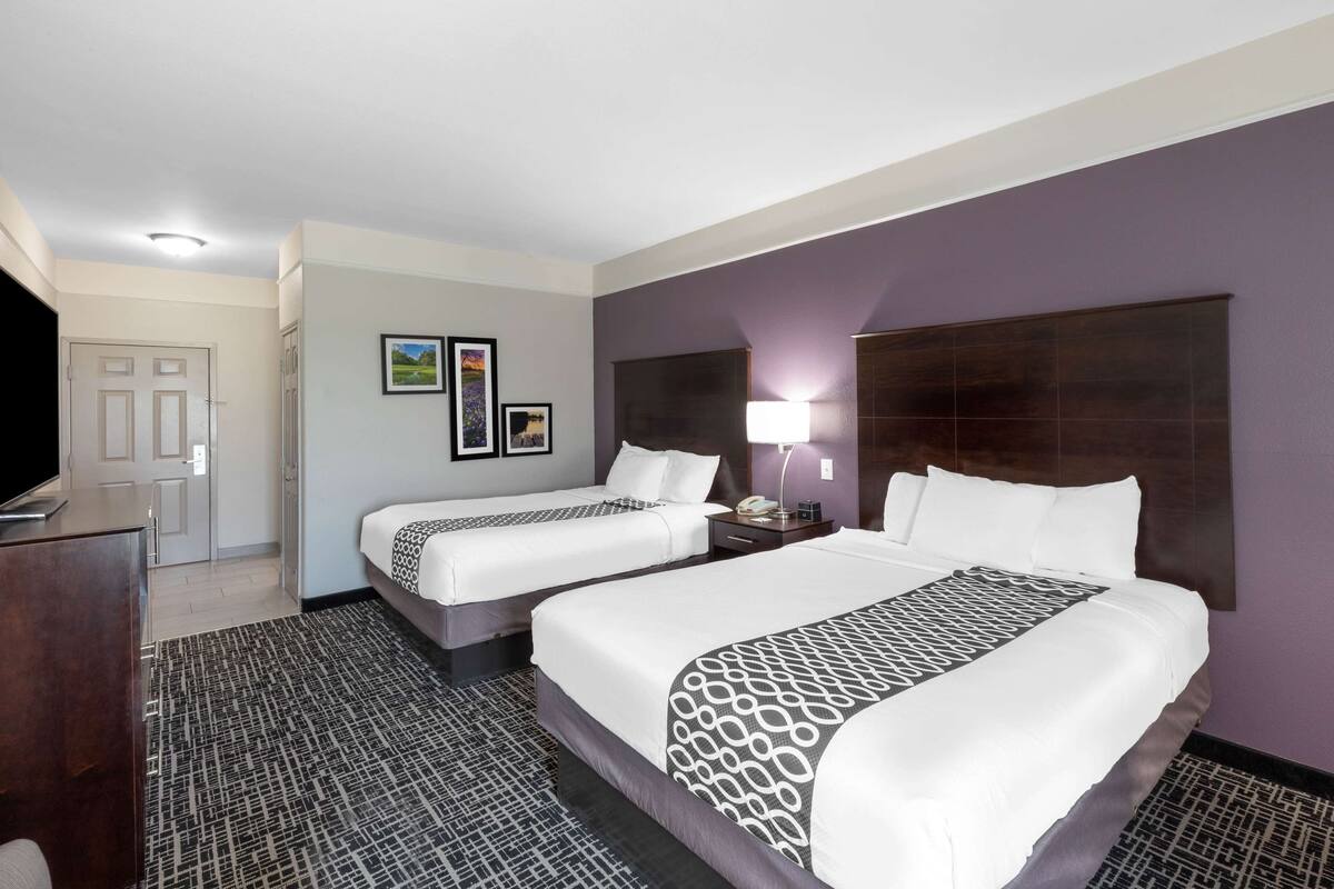 Habitación de hotel con dos camas, un escritorio, un televisor y la puerta del baño.