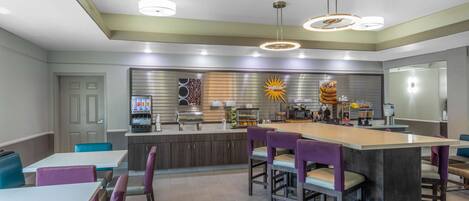 A modern kitchen with a central island, bar stools, and a dining area with tables and chairs.