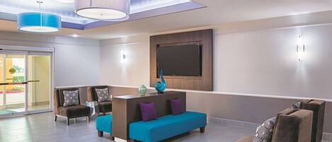 Een moderne lobby met een receptiebalie, een zithoek en een grote flatscreen televisie aan de muur.