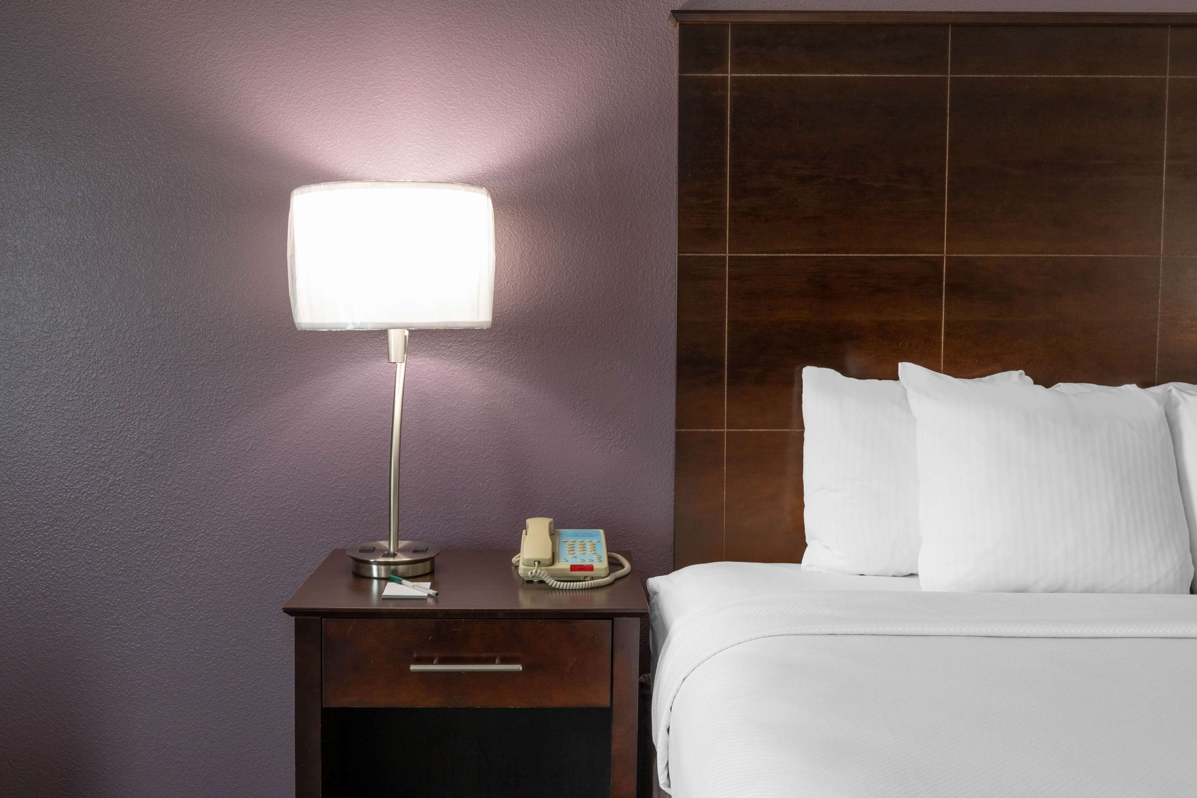 Habitación de hotel con una cama, una mesita de noche con lámpara, un teléfono y un cajón.