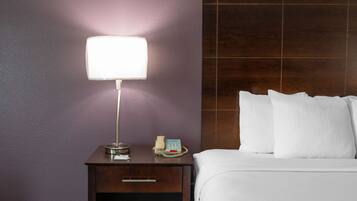 Habitación de hotel con una cama, una mesita de noche con lámpara, un teléfono y un cajón.