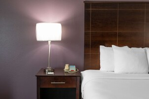 Habitación de hotel con una cama, una mesita de noche con lámpara, un teléfono y un cajón.