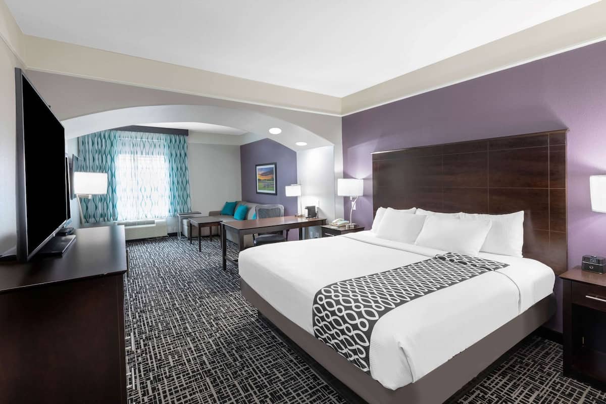 Una habitación de hotel con una cama grande, un escritorio, una silla, un televisor y una ventana con cortinas.