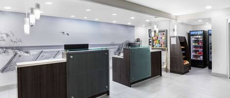 Un área de recepción moderna con un mural grande, una barra de atención y un refrigerador expositor.