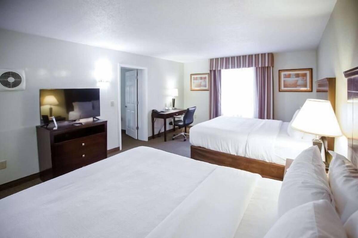 Habitación de hotel con dos camas, un escritorio, una silla, un televisor y una ventana con cortinas.