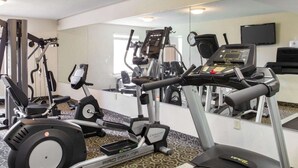 Ett gym med konditionsmaskiner, en vägg med speglar och en klocka.