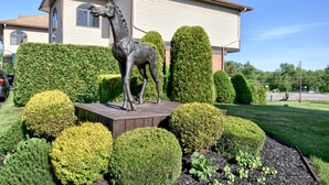 Un jardín ajardinado con una estatua de caballo, setos bien cuidados y una casa al fondo.