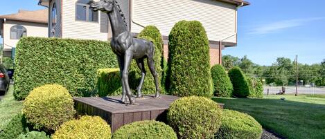 Un jardín ajardinado con una estatua de caballo, setos bien cuidados y una casa al fondo.