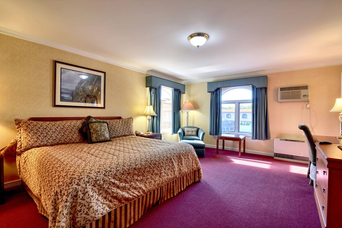 Una habitación de hotel con una cama grande, una silla, un escritorio y una ventana con cortinas.