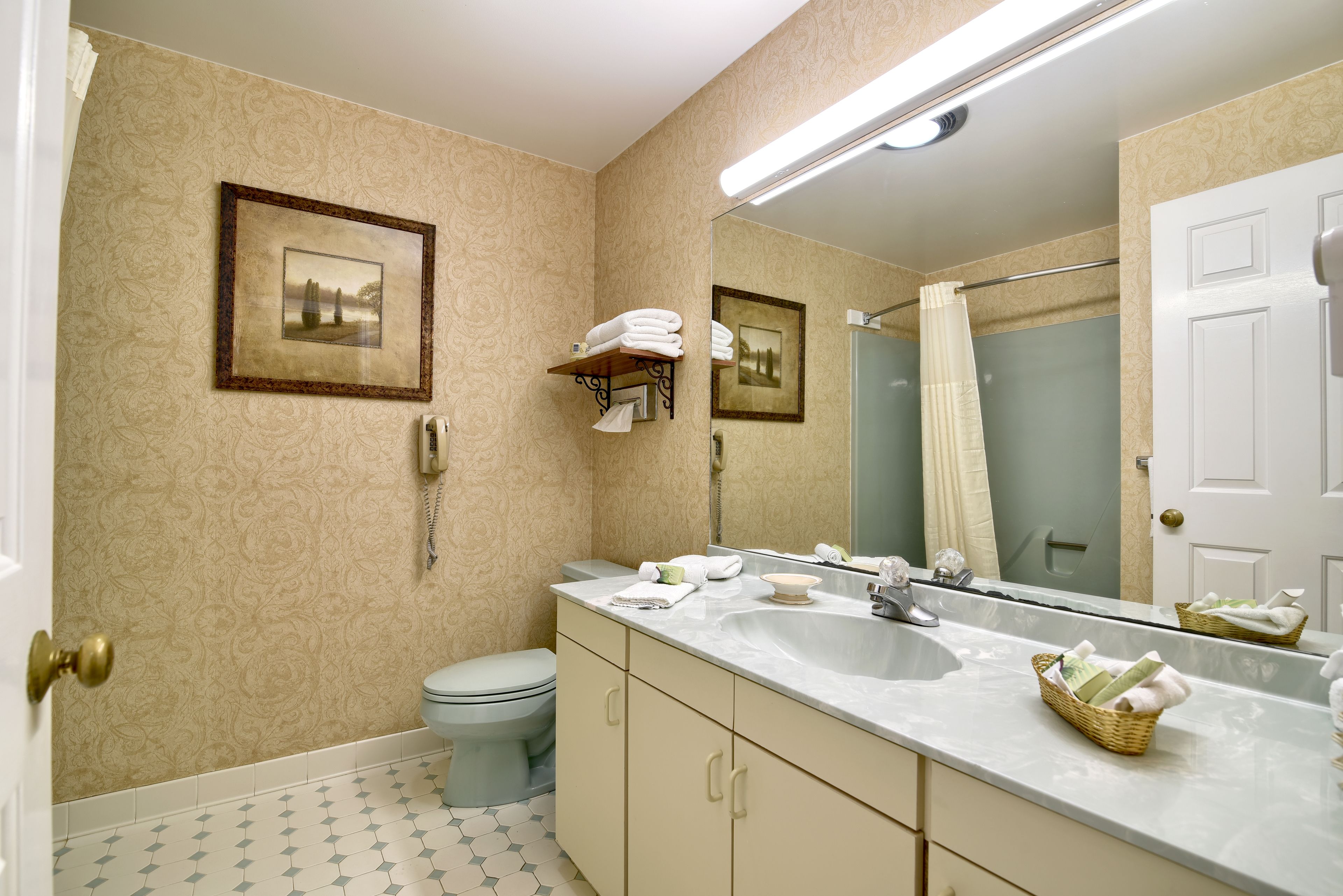 A bathroom with a toilet, sink, and mirror. There are towels and a basket on the sink counter.