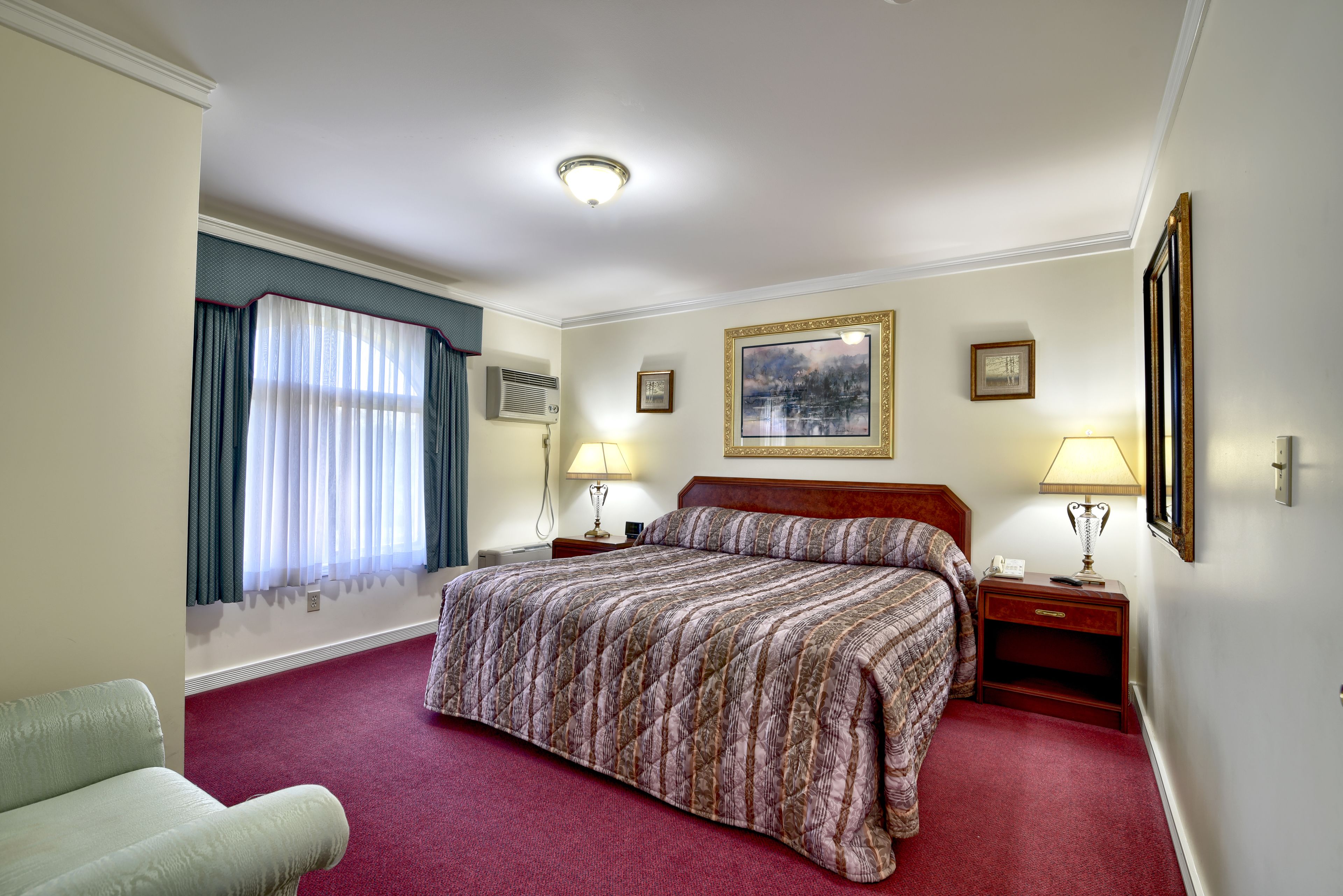Habitación de hotel con una cama grande, dos mesitas de noche con lámparas, una ventana con cortinas y un cuadro en la pared.