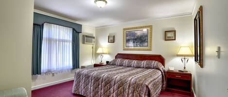 Habitación de hotel con una cama grande, dos mesitas de noche con lámparas, una ventana con cortinas y un cuadro en la pared.