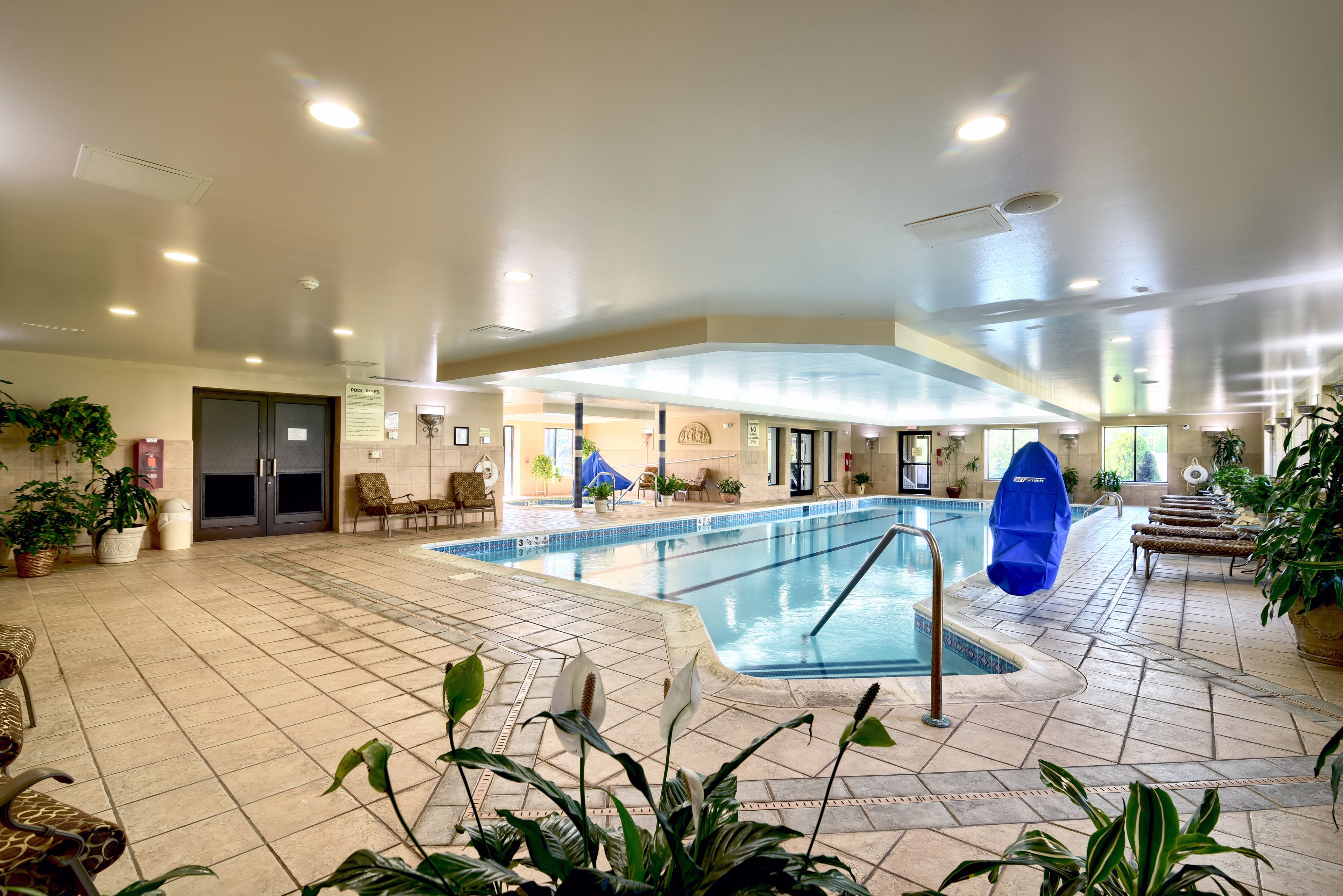 Una piscina interior con suelo de baldosas, sillas de descanso y plantas en macetas.