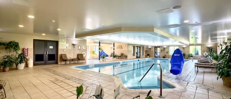 Una piscina interior con suelo de baldosas, sillas de descanso y plantas en macetas.
