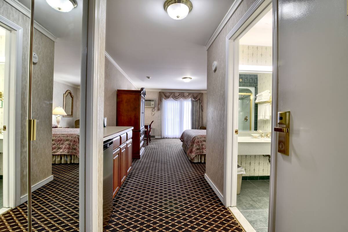 Un pasillo de hotel con alfombra estampada, una cama, un aparador y un espejo.