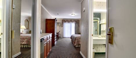 A hotel hallway with a patterned carpet, a bed, a dresser, and a mirror.