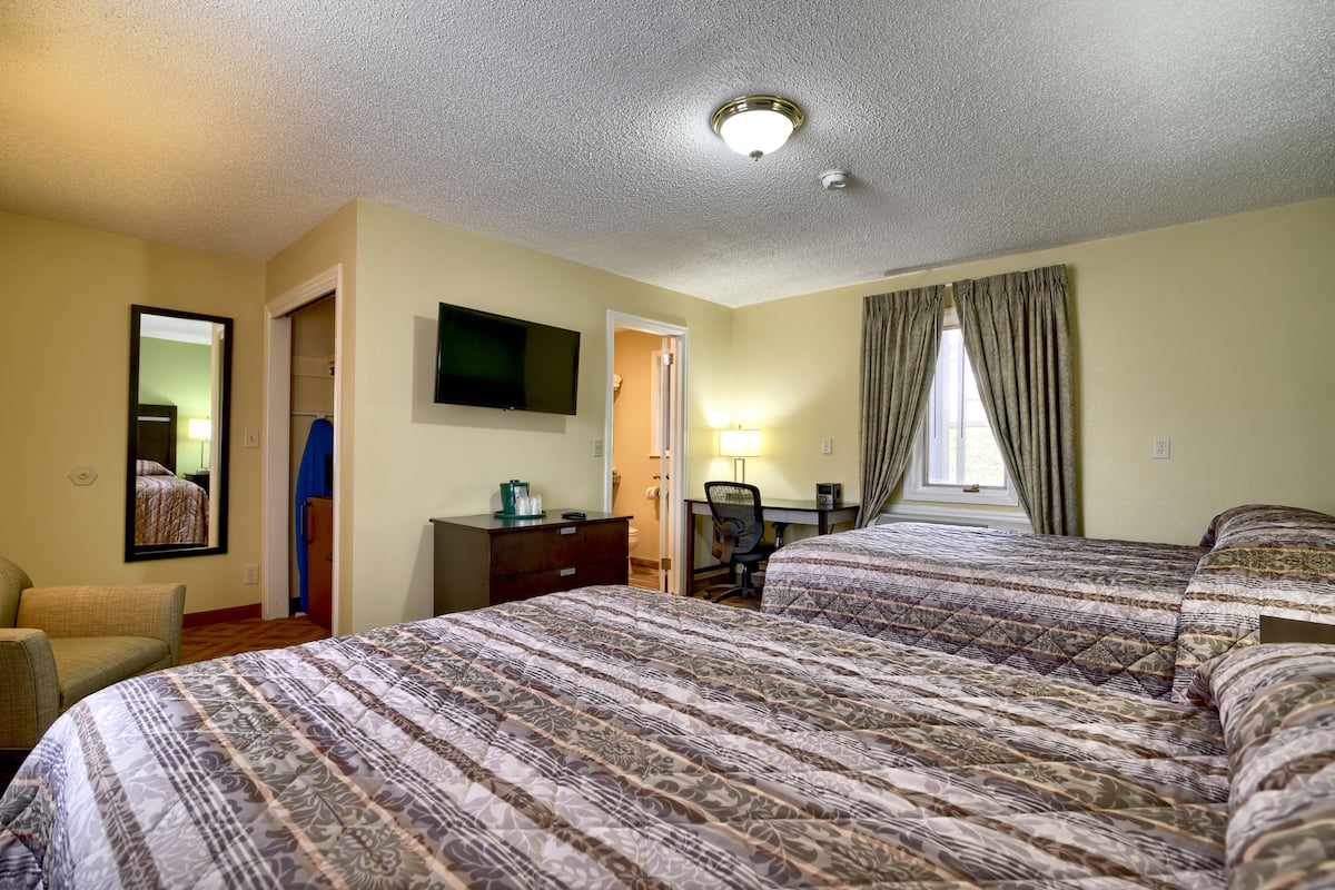 Habitación de hotel con dos camas, un escritorio, una silla, un televisor y un espejo.