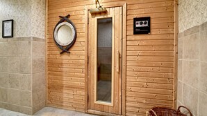 Un sauna de madera con puerta de vidrio, un espejo enmarco y un panel de control en la pared.