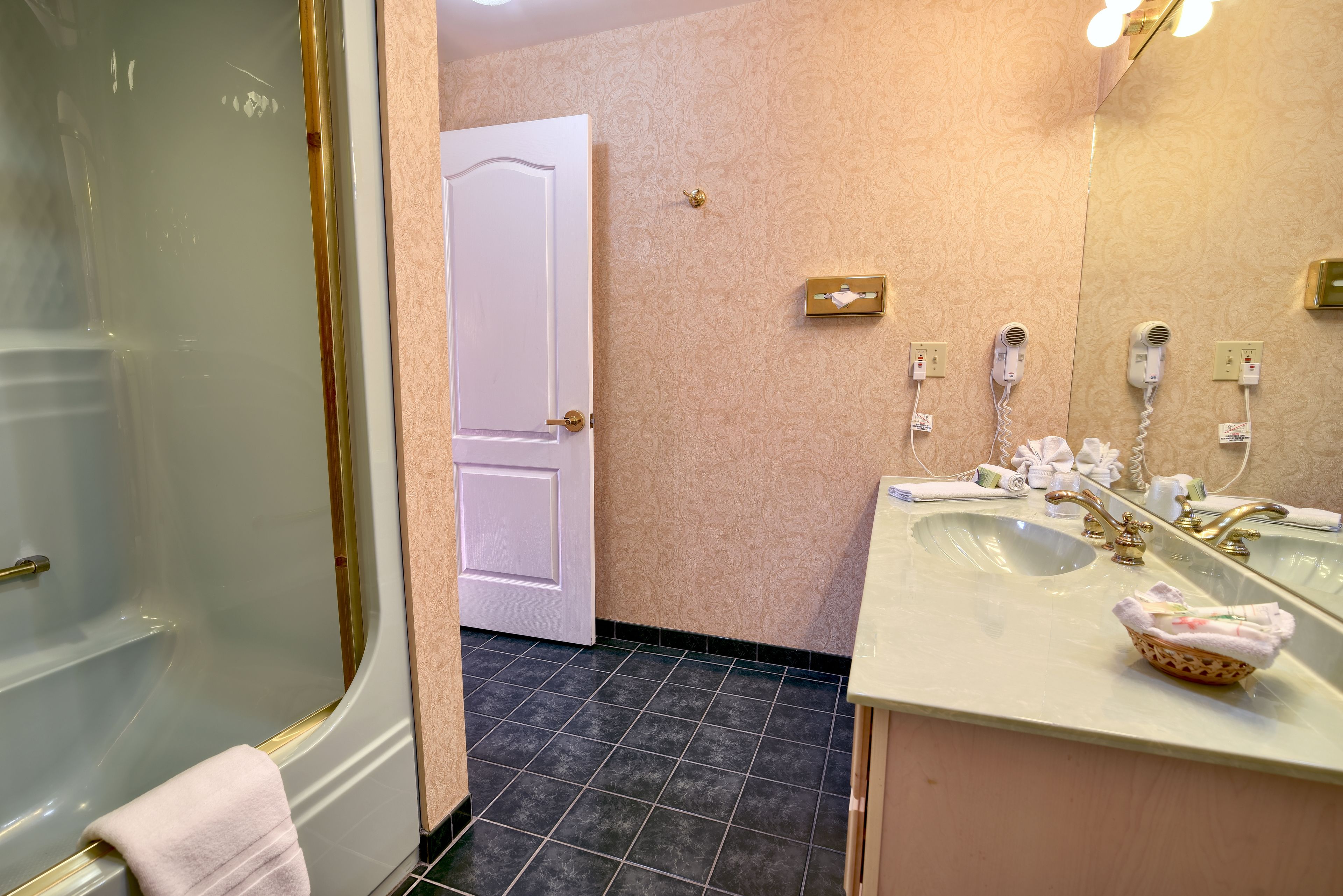 A bathroom with a glass shower enclosure, a white door, a vanity with a mirror, and two hair dryers on the wall.