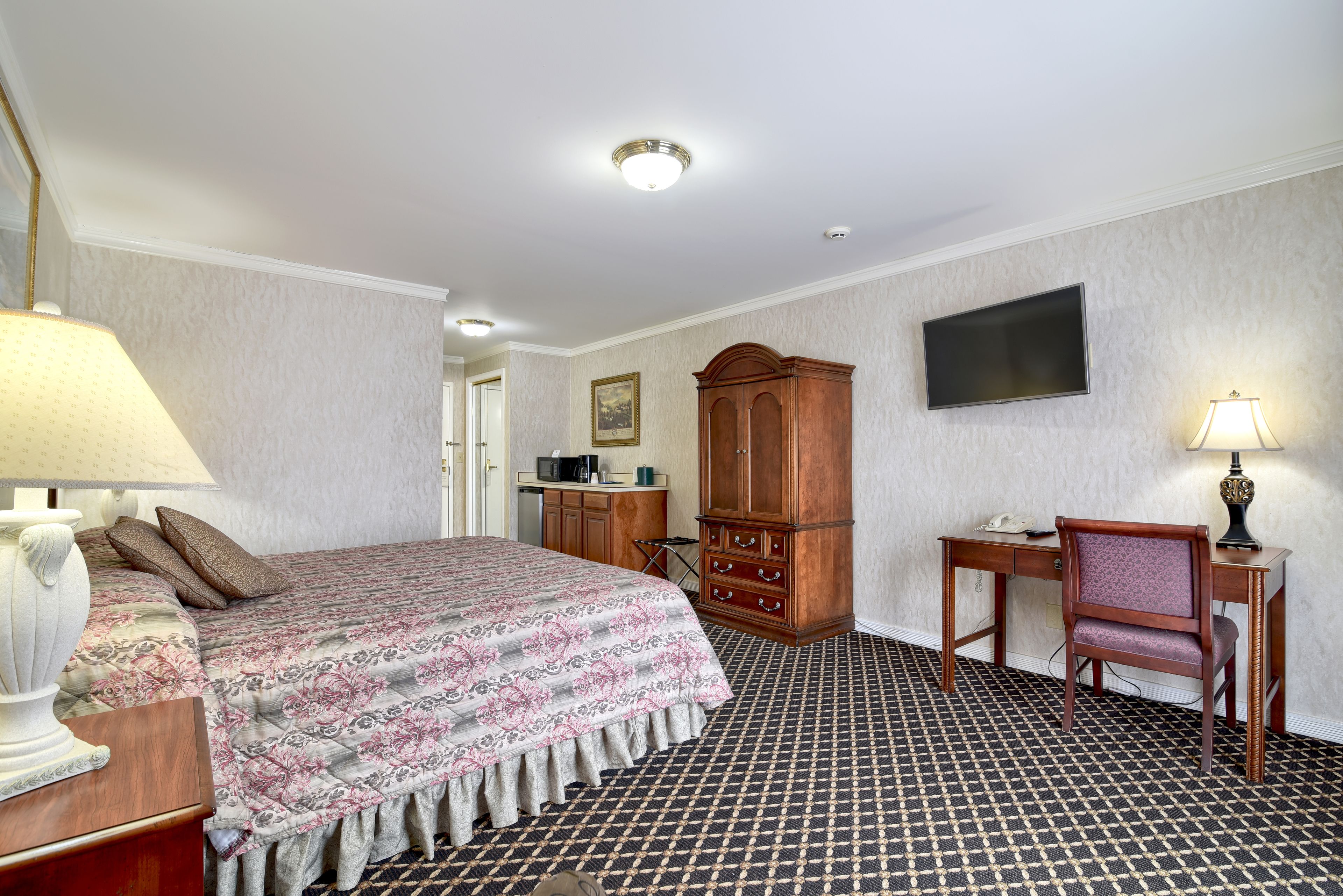 Una habitación de hotel con cama, escritorio, silla, armario y televisor.