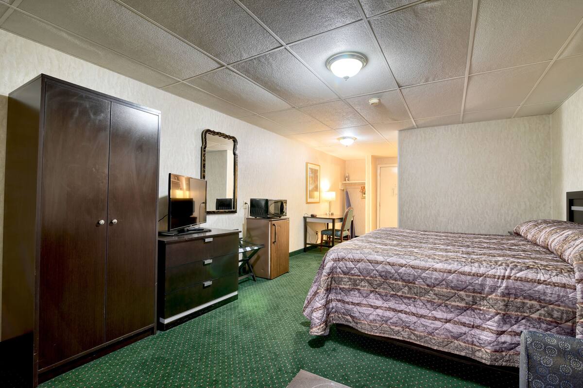 Una habitación de hotel con una cama, un aparador, un escritorio con una silla, un microondas y un televisor.