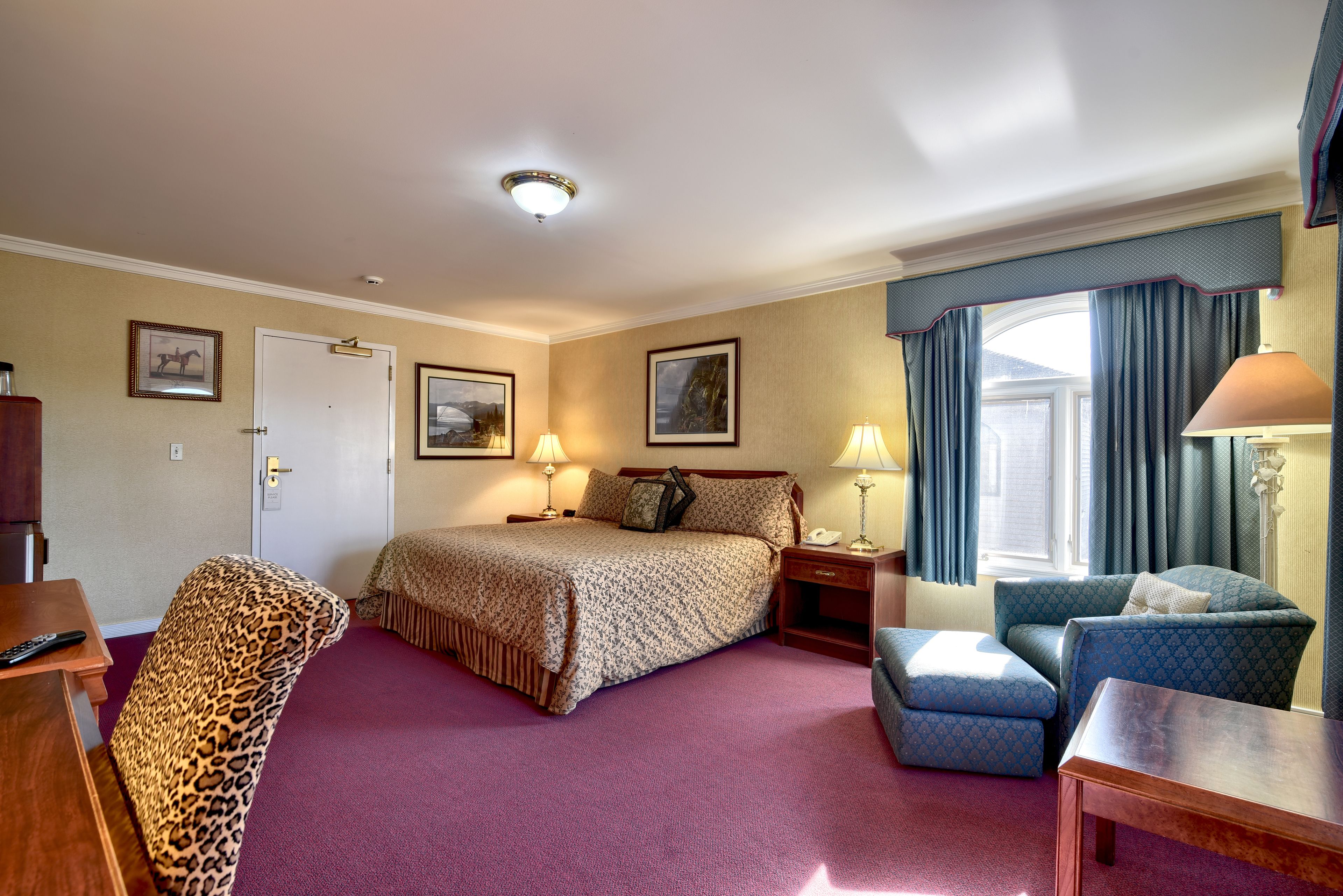 A hotel room with a bed, a desk, a chair, a lamp, and a window with curtains.
