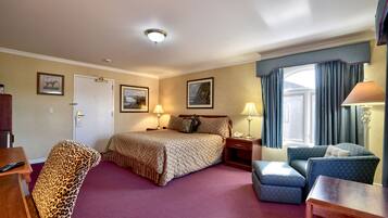 A hotel room with a bed, a desk, a chair, a lamp, and a window with curtains.