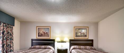 A hotel room with two single beds, a nightstand with lamps, and two framed pictures on the wall.