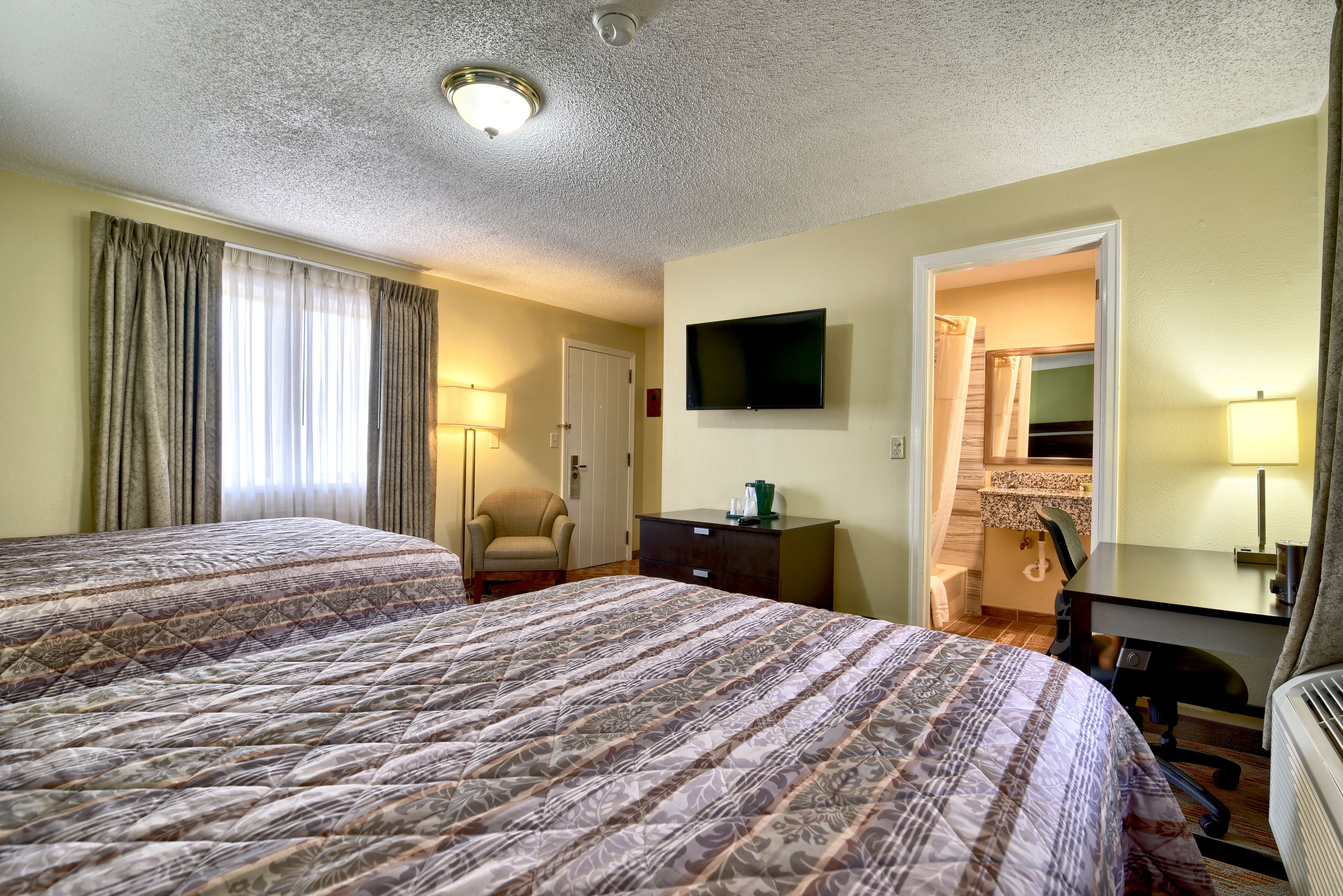 A hotel room with two beds, a desk, a chair, a TV, and a bathroom visible through an open door.