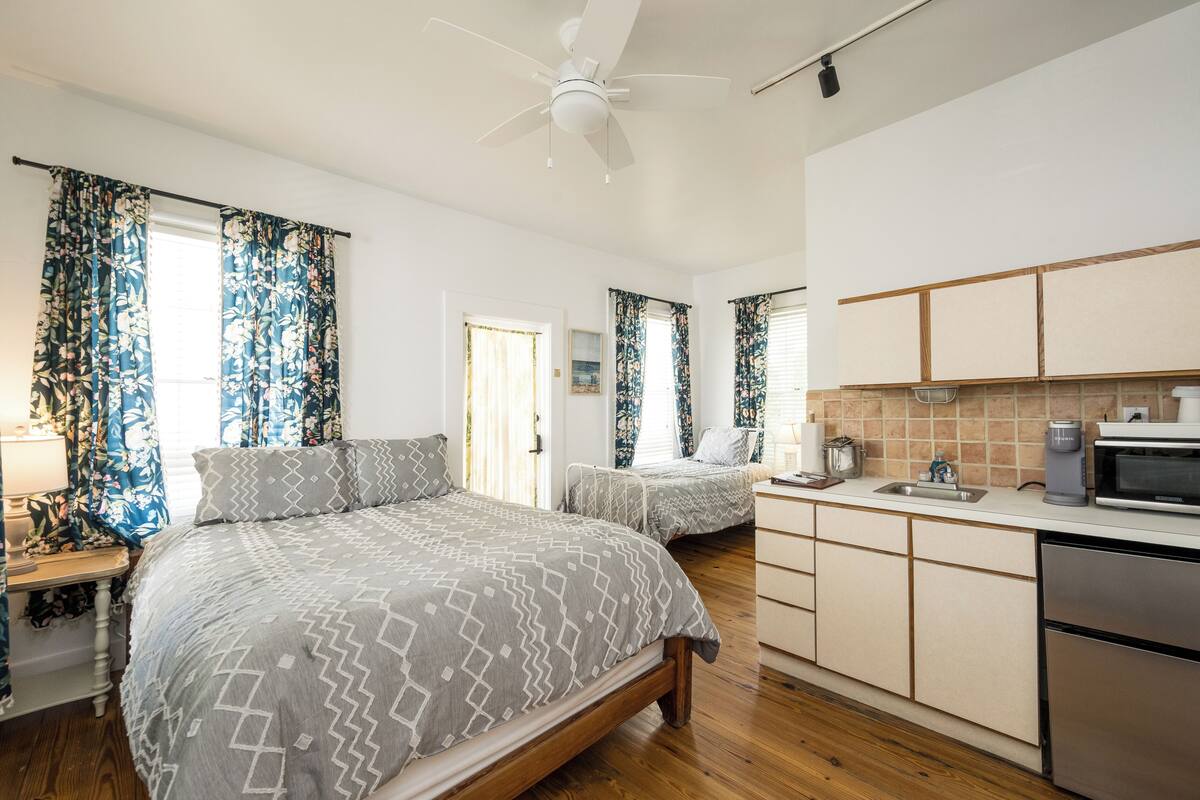 A bedroom with two beds, a kitchenette, and a ceiling fan.