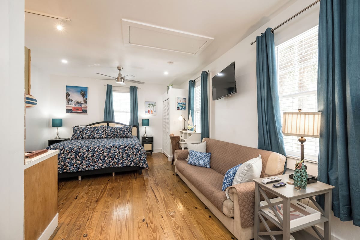 A bedroom with a bed, a sofa, a small table, a TV, and a window with curtains.