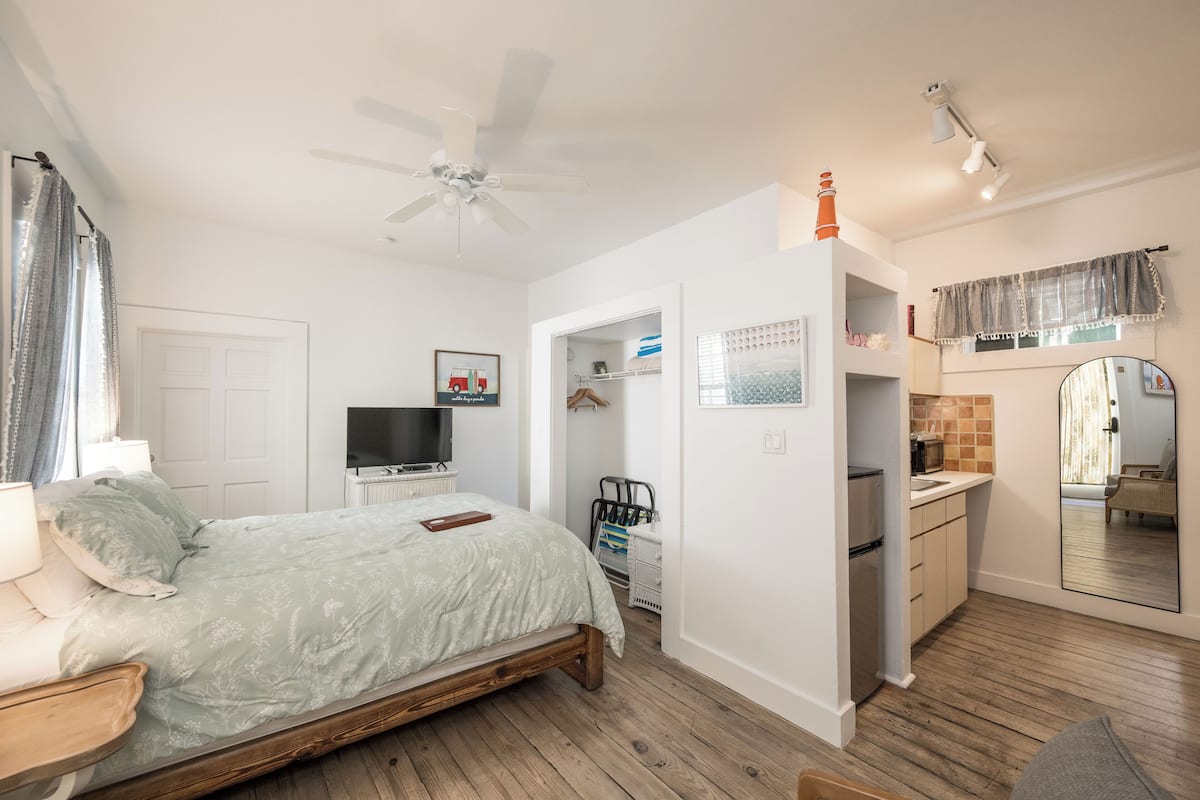 A bedroom with a bed, a TV, a ceiling fan, and a bathroom with a mirror and sink.