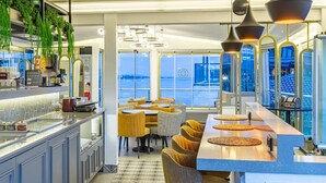 A modern restaurant with a bar area, seating with yellow chairs, and large windows offering a view of the water. - Best Point Hotel (Istanbul)