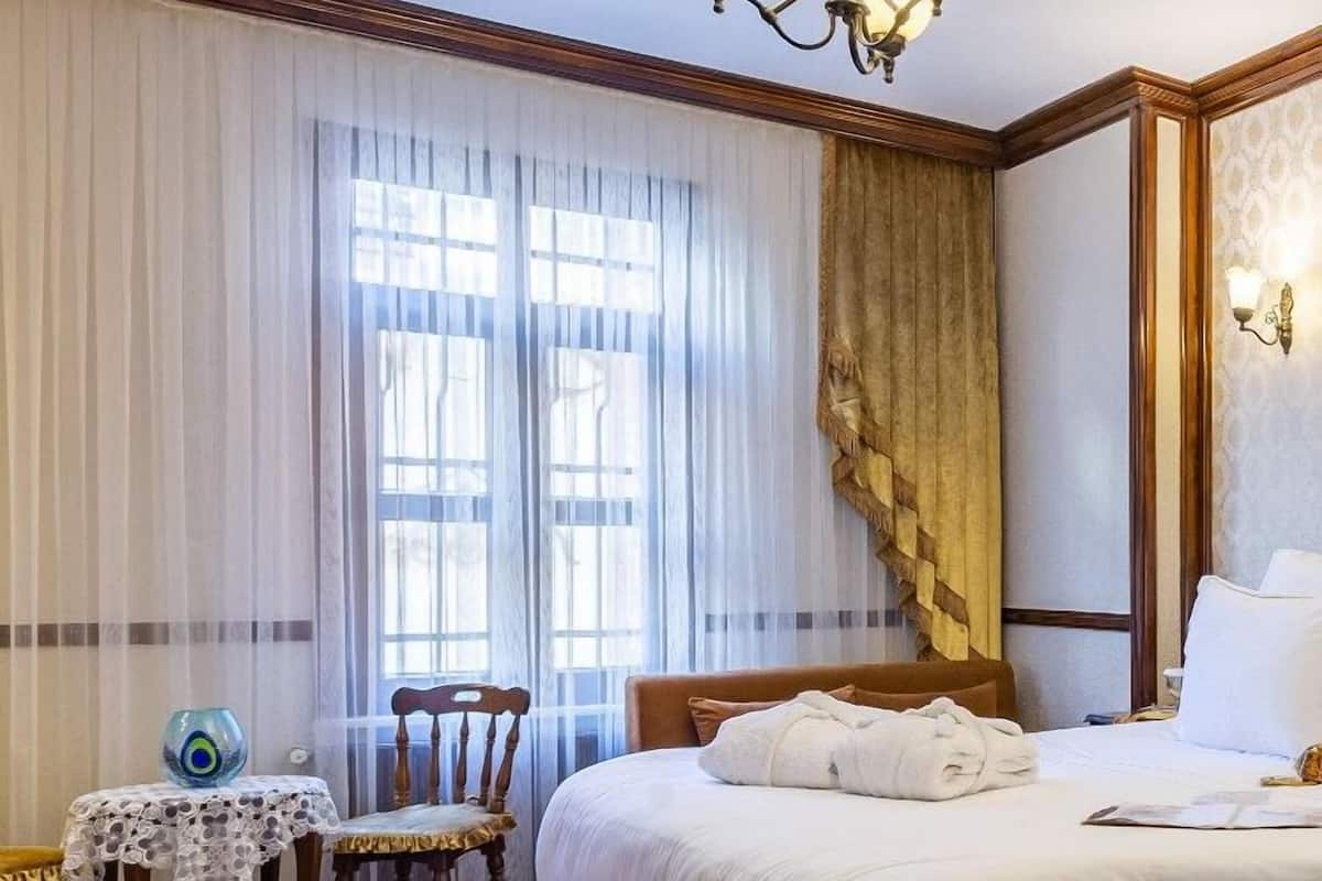 A hotel room with a large bed, a wooden bench, a small table with a vase, and a chandelier.